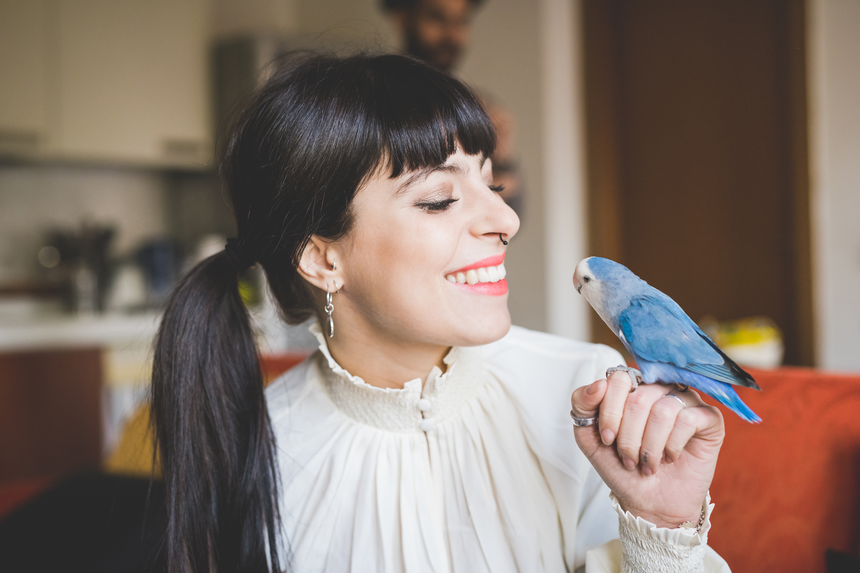 Woman smiles at her pet bird perched on her finger