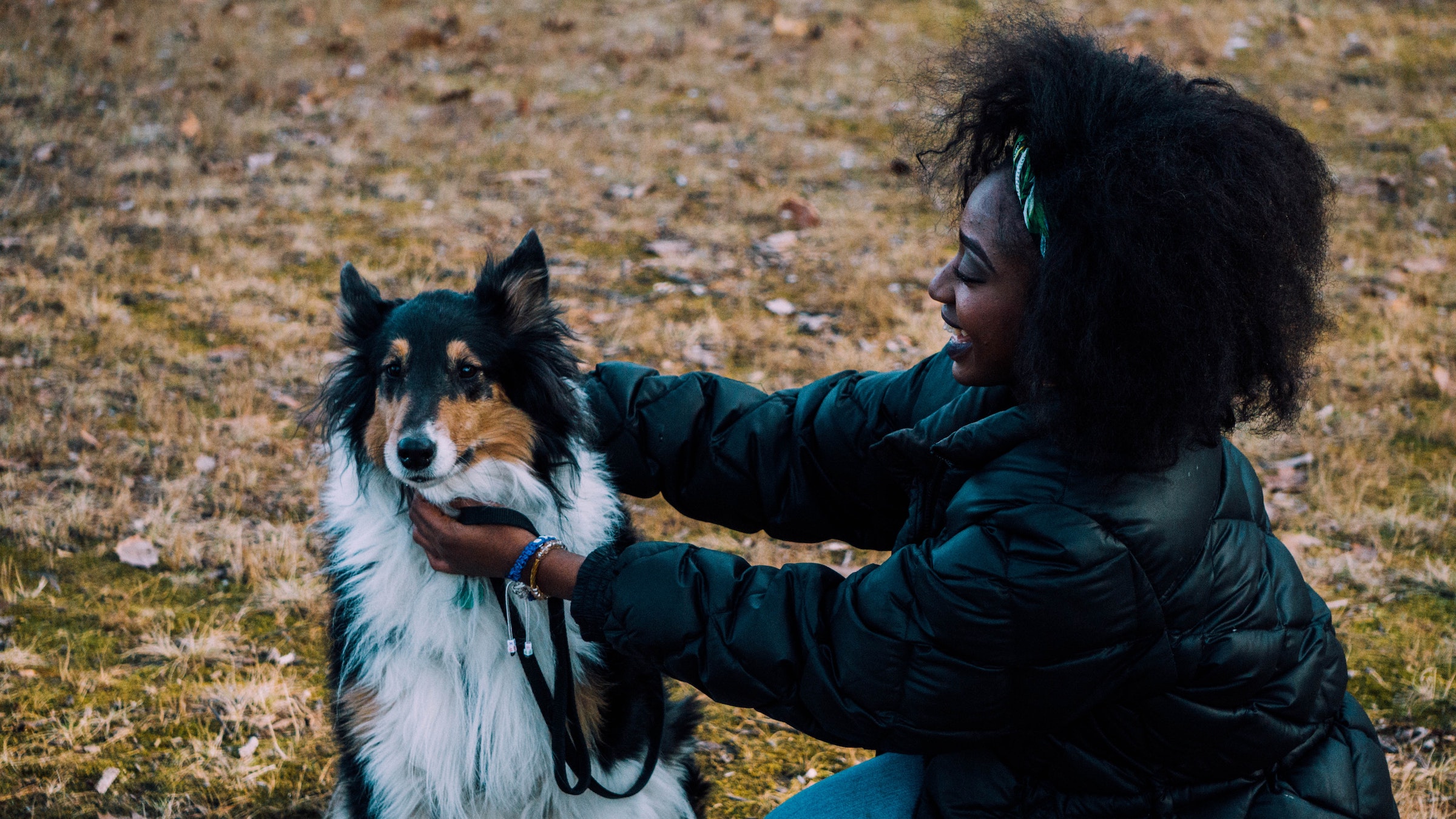 A woman pets a Collie dog while the two stand outside
