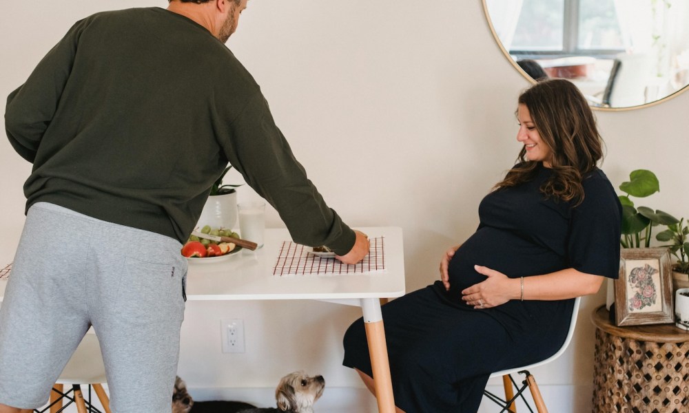 a man serving pregnant woman in black dress food with dog underfoot